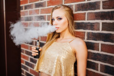 Vaping. Young beautiful girl smoking ( vaping ) e-cigarette with smoke outdoors. Vapor concept.