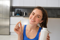 Close up portrait of smiling, healthy young woman, holding tablets, taking vitamin dietary supplements after home fitness workout